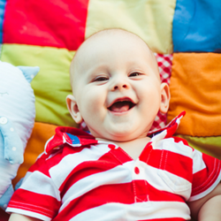 smiling happy baby lying on its back on a colourful quilt