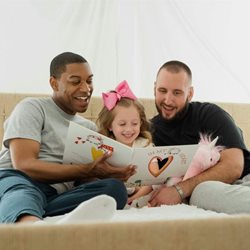 Two people reading a book on a couch with a young girl